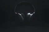 Dark, cinematic shot of headphones resting on a sleek black surface with subtle blue highlights.