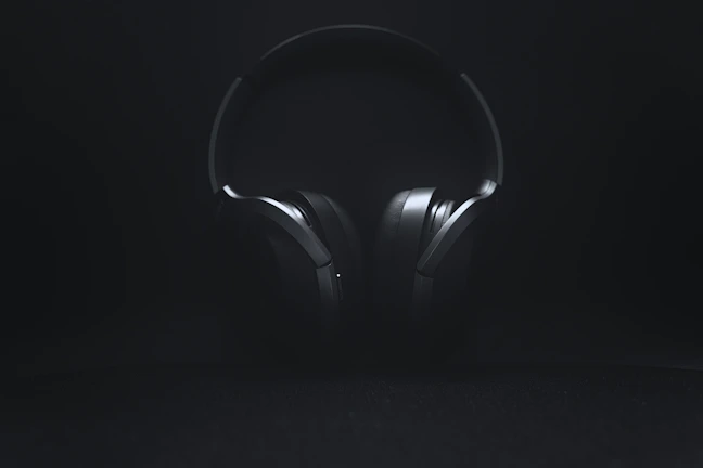 Dark, cinematic shot of headphones resting on a sleek black surface with subtle blue highlights.