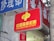 A red sign displaying the text 'China Welfare Lottery' in both Chinese and English, mounted on the exterior of a building. The surroundings include a blue sign with Chinese characters and a partial tree trunk visible on the right side.