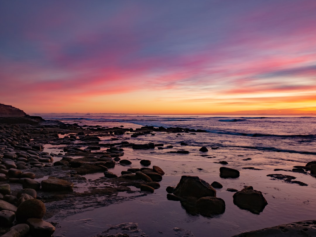 rocks near seashore under orange sky,