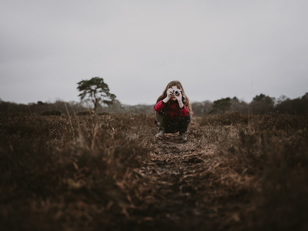 selective focus photography of girl sitting on farm road holding camera