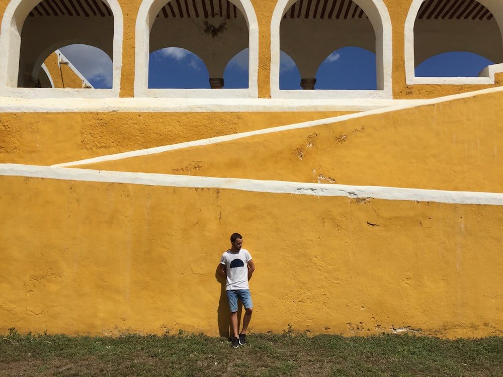 man in white shirt leaning on yellow concrete wall during daytime