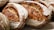 Several loaves of artisanal bread with a rustic, golden-brown crust. The bread features a dusting of flour and visible seeds embedded in the crust, creating a textured appearance.