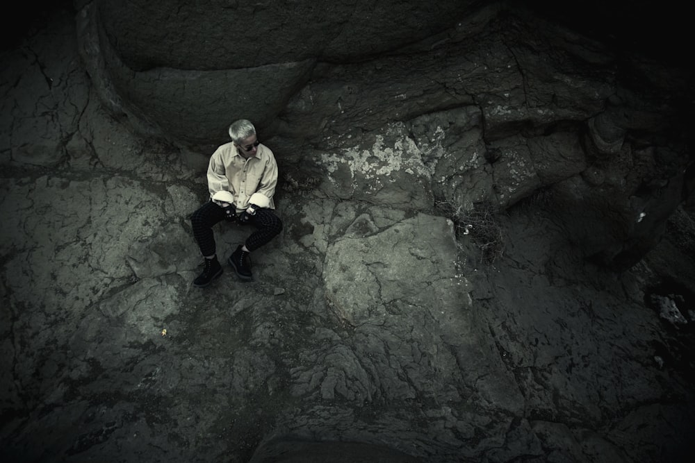 man sitting on ground beside rock