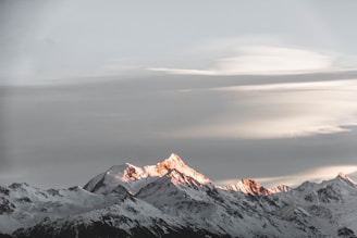 Sunset casting golden light on snow-capped peaks with a lone climber silhouetted against the sky.