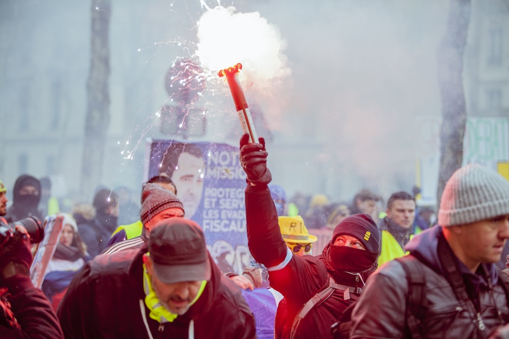 person in black jacket stands beside person holding firecracker