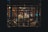 An intimate setting inside a dimly lit restaurant with ornate decorations. Tables and chairs are arranged around a central area, where several people are seen conversing or dining. Wooden structures and decorative elements lend an elegant and traditional atmosphere.