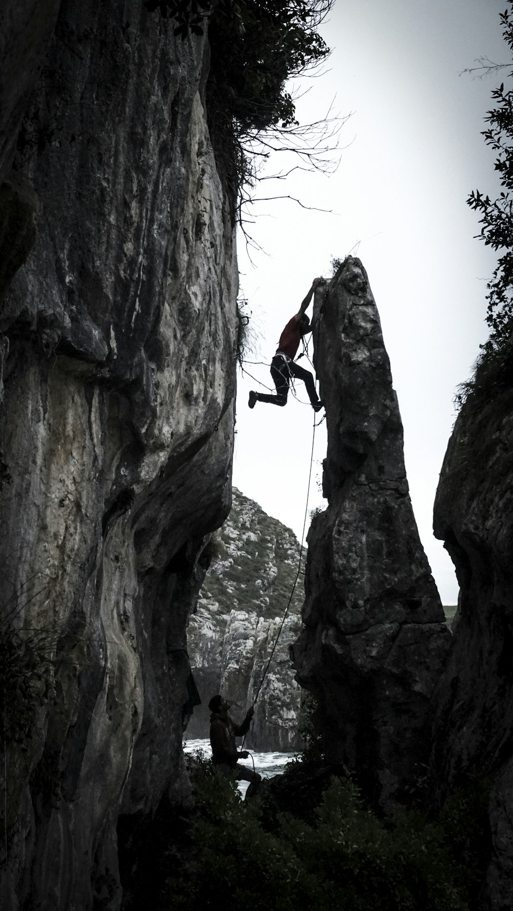 grayscale photography of man climbing rock