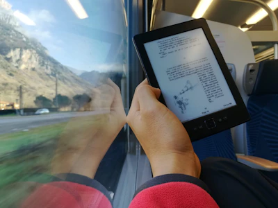 A person reading an e-book on a tablet while traveling, with a scenic background.