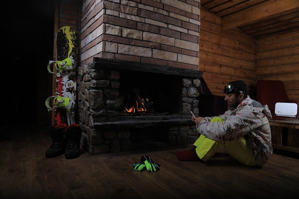 man holding smartphone sitting on brown floor near the fireplace inside a room