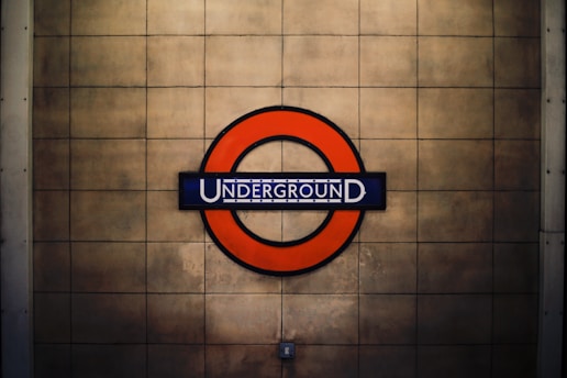 A circular red sign surrounds a blue bar with the word 'UNDERGROUND' in white, set against a beige tiled background.