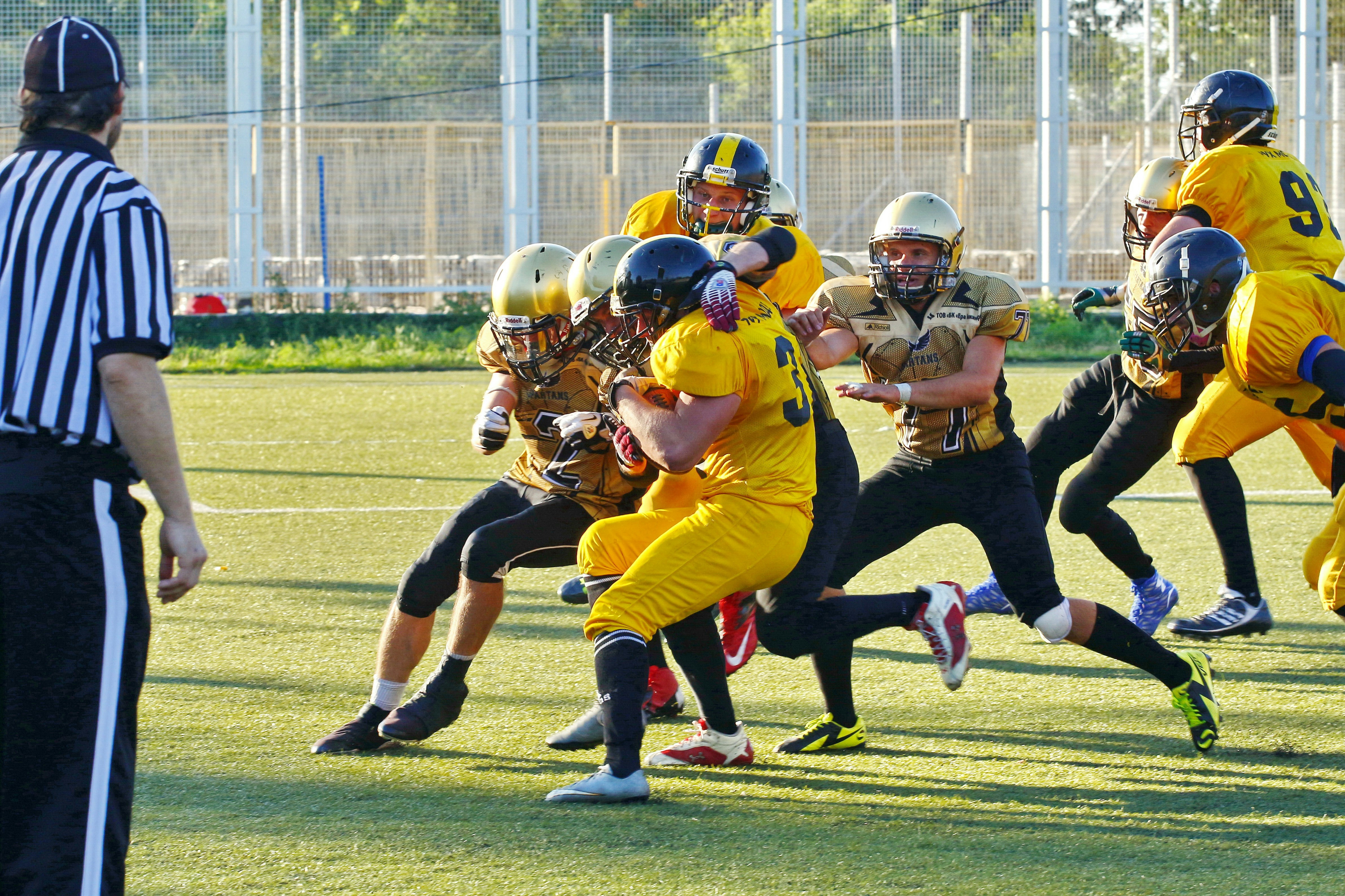 people playing american football with referee on the field during daytime