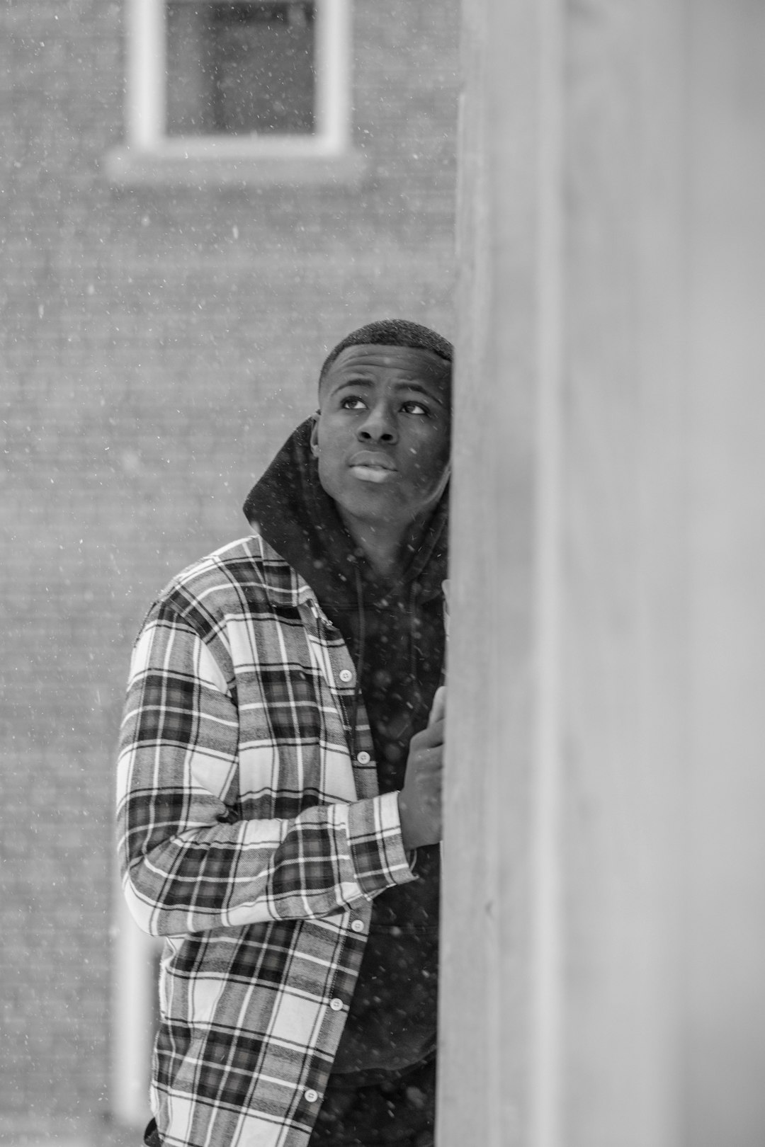 greyscale photo of man wearing plaid dress shirt leaning on wall