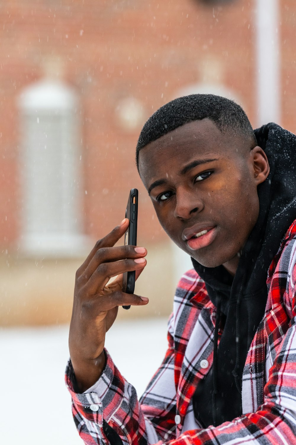 man in pink, white and red plaid dress shirt sitting and holding phone