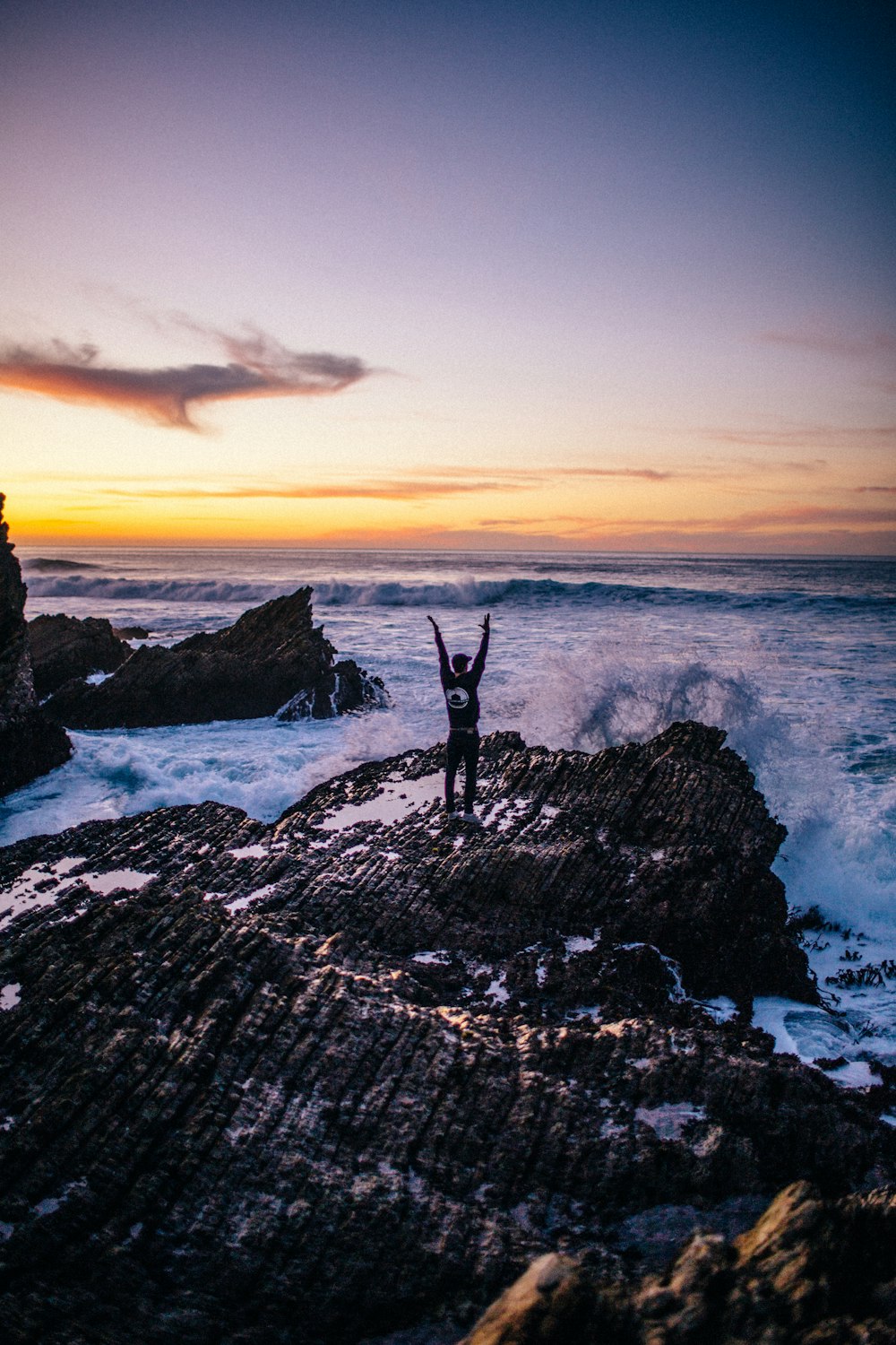 person standing on rock formation near sea during sunset