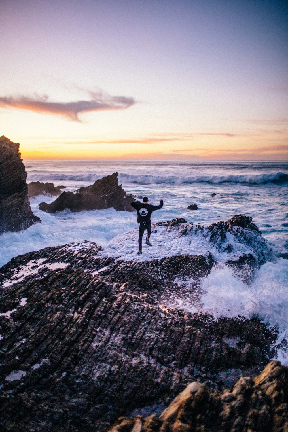 man jumps on rock while water splashes on him at the beach