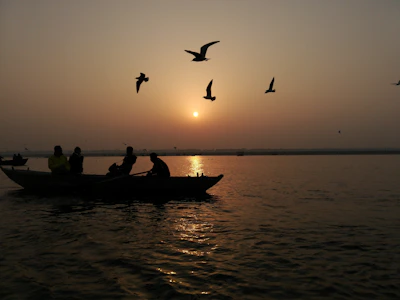 A group of friends laughing together on a wooden boat drifting along a calm lake at sunset.