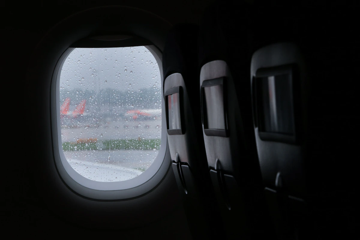 Traveler watching storm clouds and a departing plane through an airport terminal window