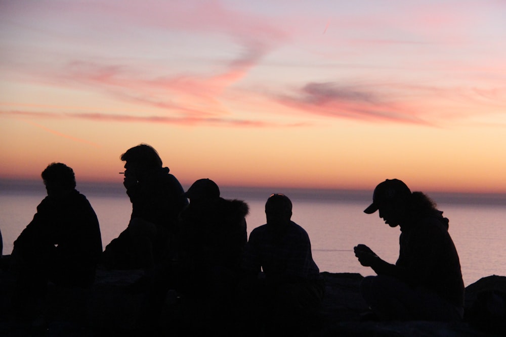 silhouette of people sitting near body of water