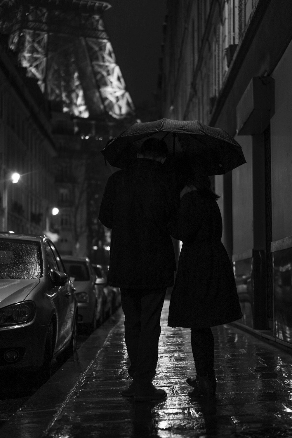 grayscale photography of man and woman standing under umbrella
