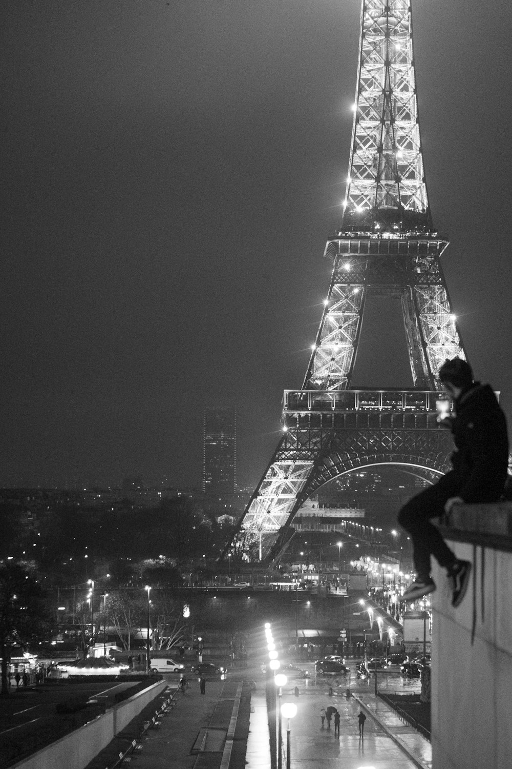 grayscale photo of man sitting on rooftop near Eiffel Tower, Paris