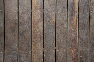 Wooden planks arranged vertically with visible grain and texture. The wood appears weathered, with variations in color and some small nails or fasteners visible.