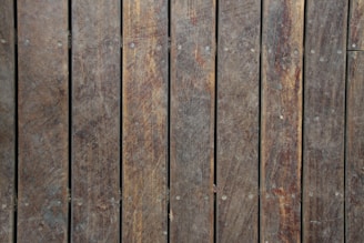 Wooden planks arranged vertically with visible grain and texture. The wood appears weathered, with variations in color and some small nails or fasteners visible.