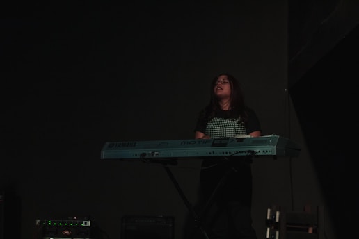 A person is playing a Yamaha electronic keyboard in a dimly lit environment. The focus is on the musician, who appears to be concentrating, possibly deeply engaged in the music. The background is dark, highlighting the musician and the instrument.