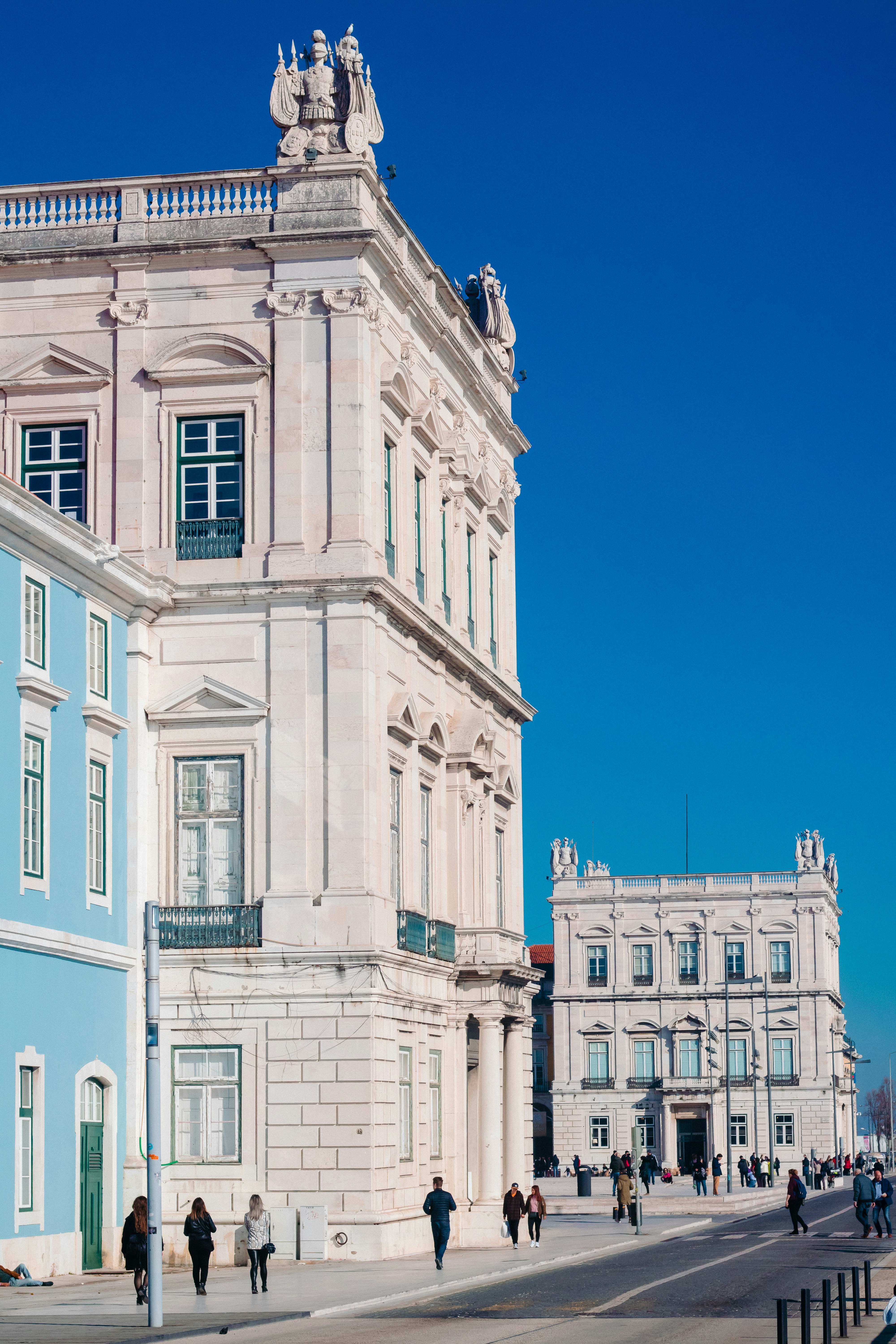 昼間、白いコンクリートの建物の横を歩く人々