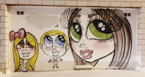 The image features a vibrant mural depicting three stylized cartoon characters with exaggerated features such as large eyes and big smiles. The characters are painted on a white tiled wall, adding a playful and whimsical vibe.