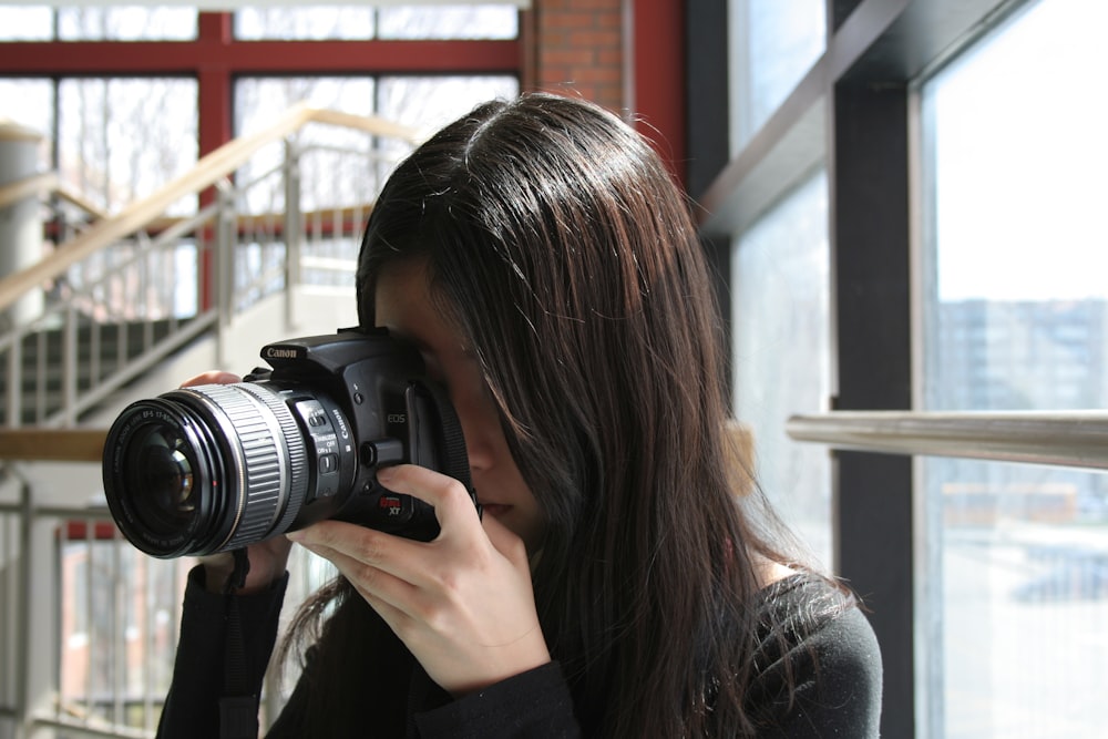 woman standing near window using DSLR camera