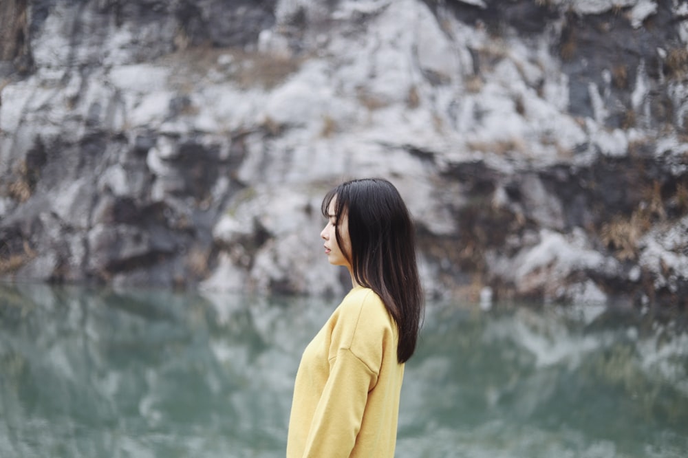 woman in yellow standing beside body of water