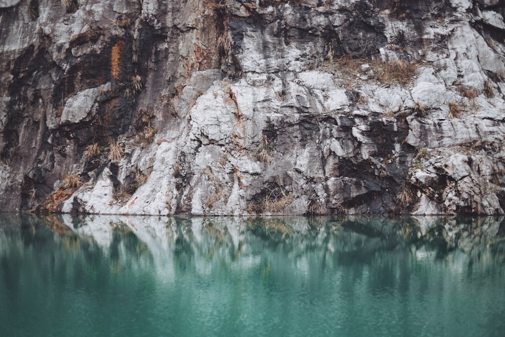 green calm body of water beside brown rock wall