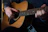 A person is playing an acoustic guitar, gently strumming the strings with their right hand while their left hand holds the neck of the guitar.