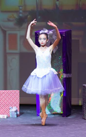 A birthday girl crowned as 'balerinų karalienė' smiling proudly on a small stage with a tiara and tutu.