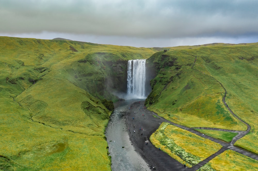 raging falls in between green and yellow grass covered mountains