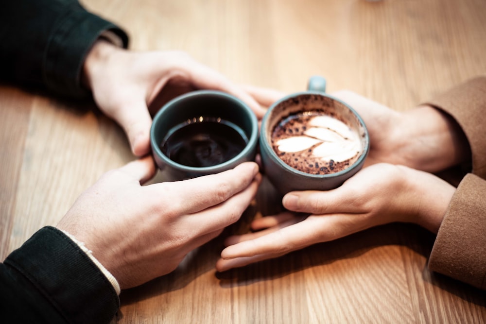 duas pessoas segurando canecas de cerâmica com café