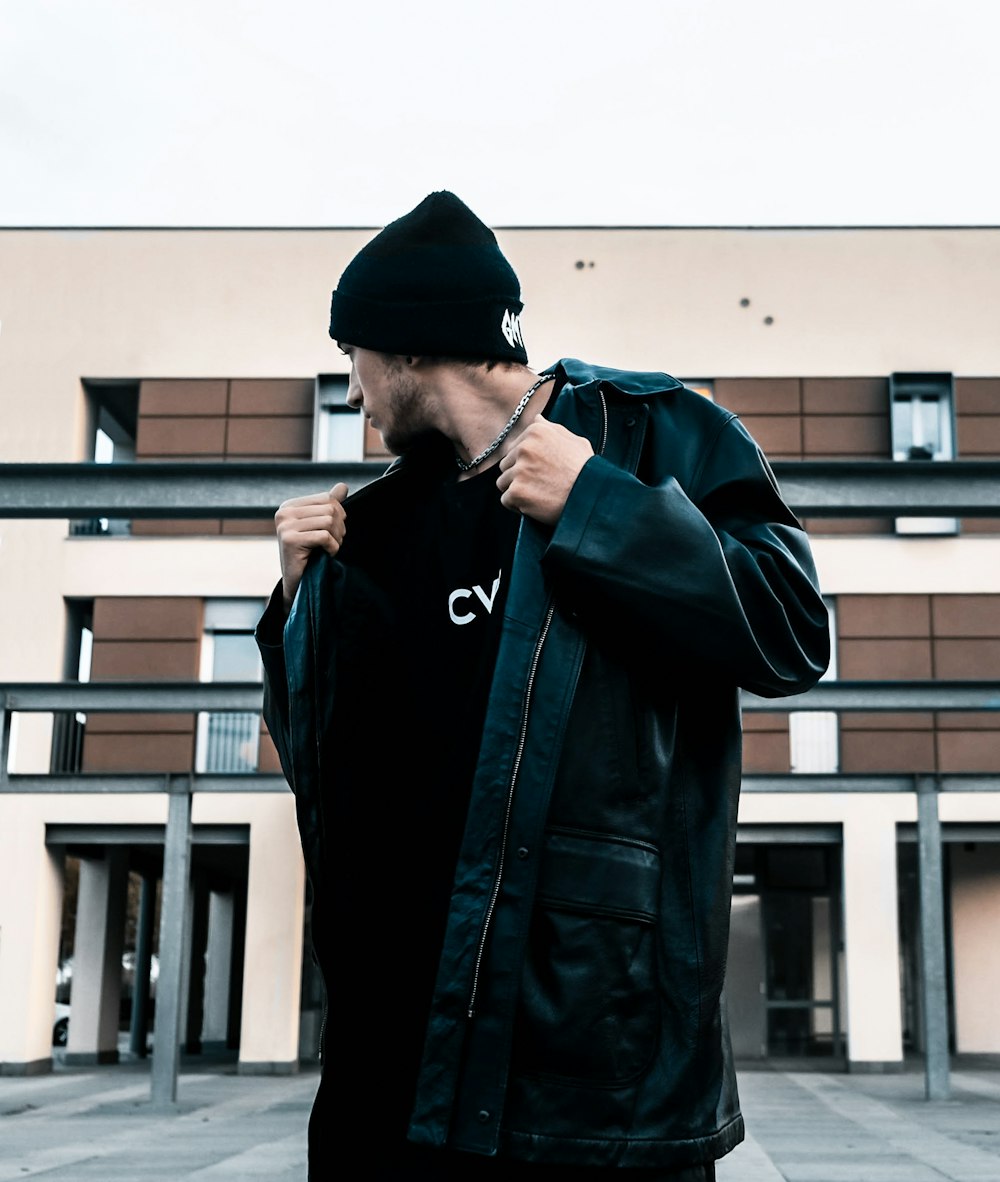 man in black leather jacket standing near beige building