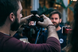 man taking video of standing man wearing black crew-neck top