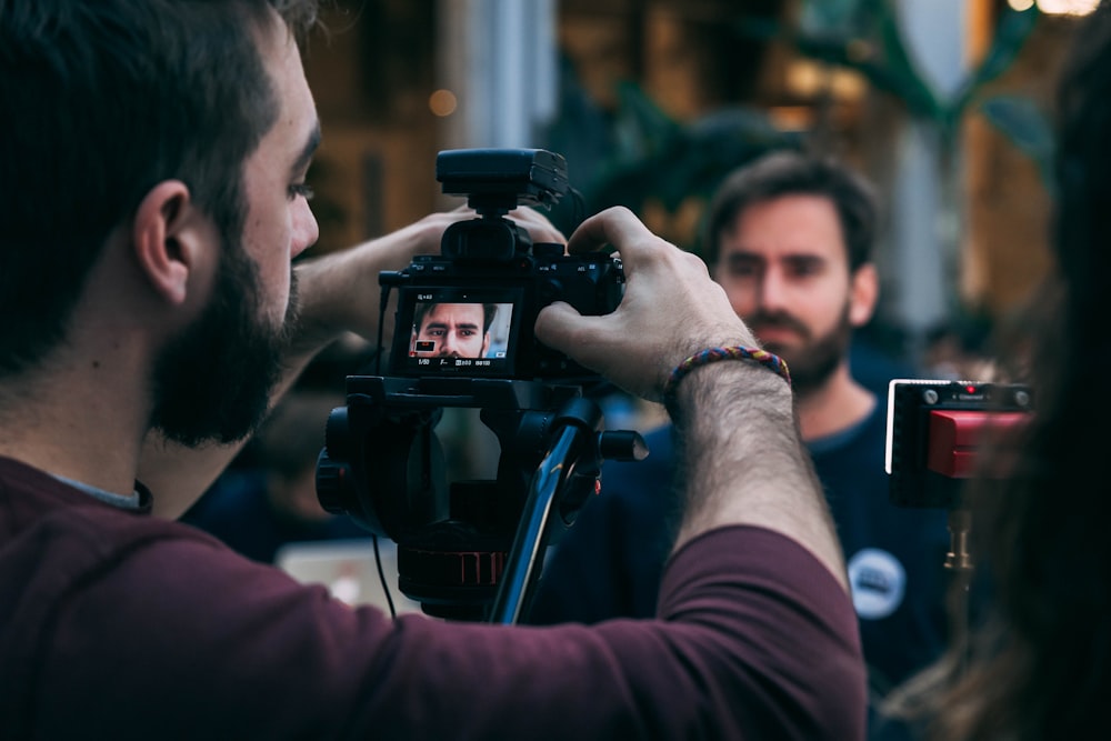 man taking video of standing man wearing black crew-neck top