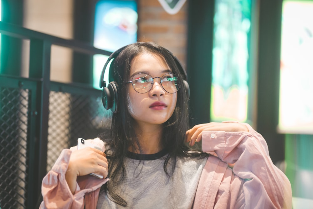 selective focus photography of woman holding smartphone and wearing headphones