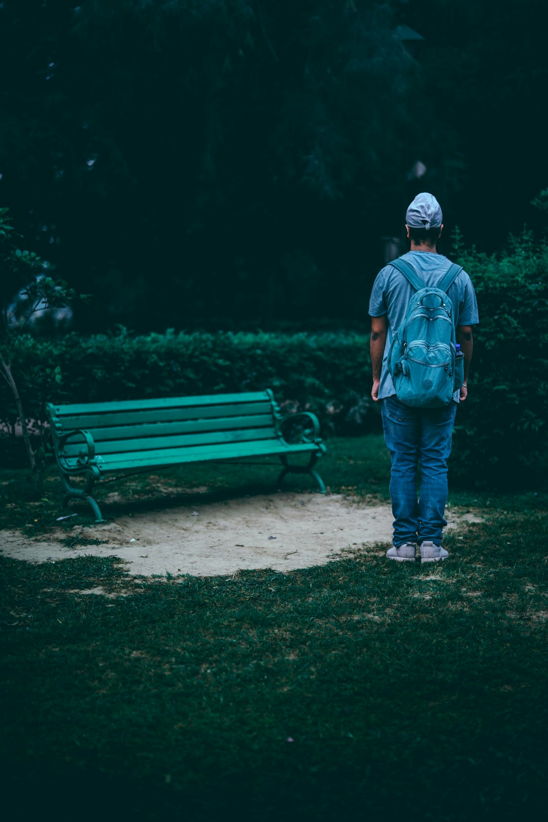 person in teal shirt stands in front of park bench