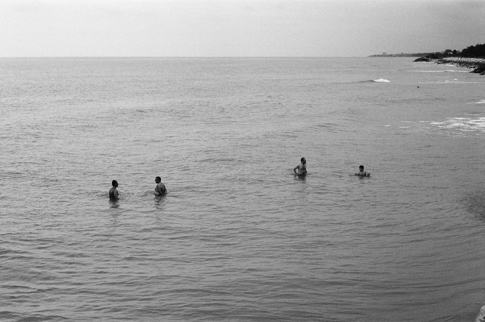 4 people wading at sea grayscale photo
