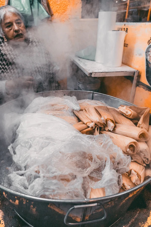 Tamales wrapped in corn husk steaming in a large pot