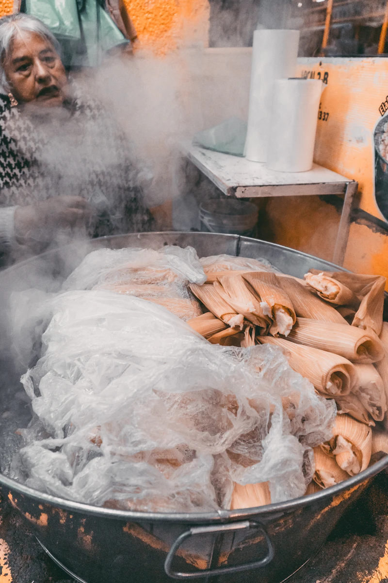 Tamales wrapped in corn husk steaming, prepared fresh at the market