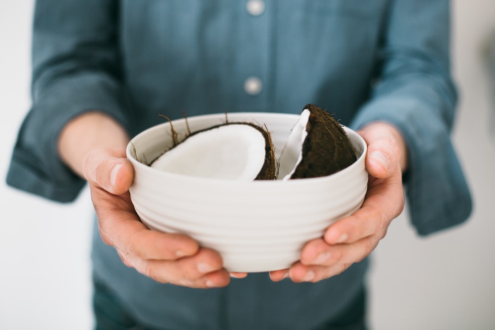 person holding white ceramic bowl with halved coconut