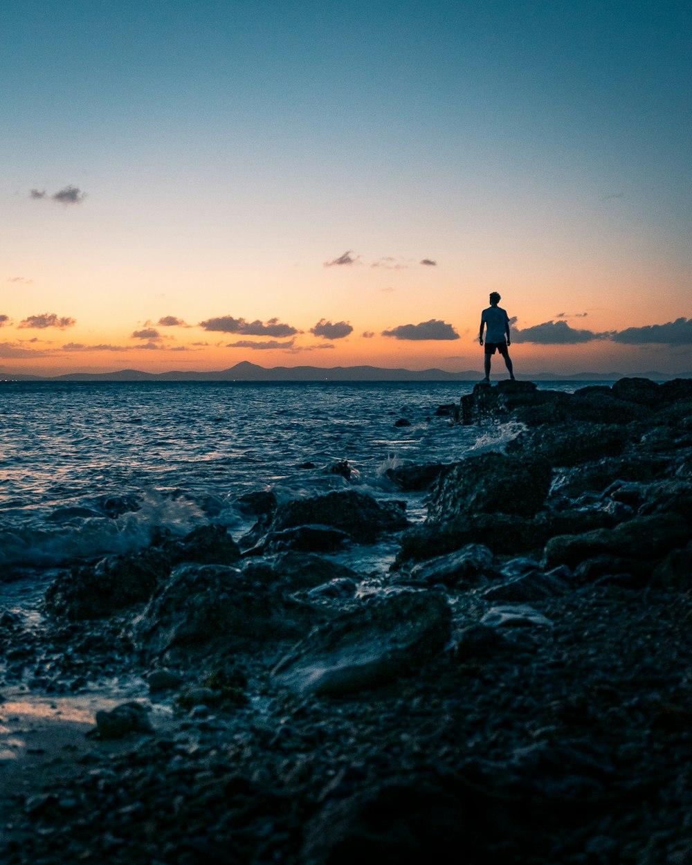 person standing on rock beside body of water during daytime