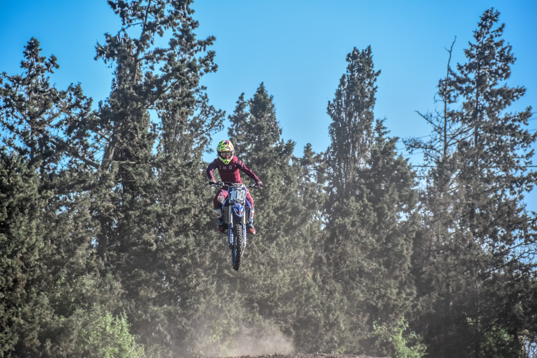 person riding motocross dirt bike in front of green trees