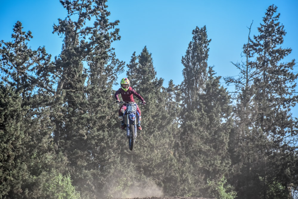 person riding motocross dirt bike in front of green trees
