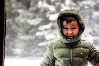 A joyful child wearing a Christmas-themed hoodie with a smiling snowman graphic, playing in the snow.